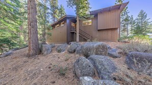 A cabin with a wooden exterior, a staircase leading to a deck, and a forested backdrop. - Central 3 Bedroom House Less Than a Mile to Heavenly (South Lake Tahoe)