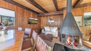 A cozy cabin interior with a wooden dining table, cushioned seating, a fireplace, and a television mounted on the wall. - Central 3 Bedroom House Less Than a Mile to Heavenly (South Lake Tahoe)