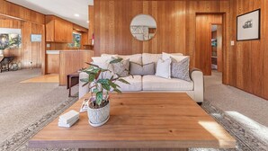 A living room with a wooden panel wall, a round mirror, a beige sofa, and a coffee table with a potted plant. - Central 3 Bedroom House Less Than a Mile to Heavenly (South Lake Tahoe)