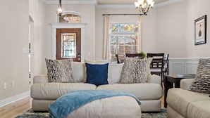 A living room with a beige sectional sofa, patterned throw pillows, a blue throw blanket, and a chandelier.