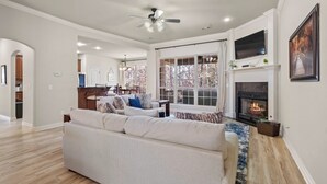 A spacious living room with a large white sofa, a fireplace, and a television mounted above it.
