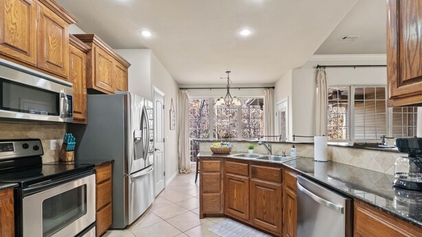 A modern kitchen with wooden cabinets, stainless steel appliances, and a large window with a view of trees.