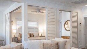 Ein Zimmer mit einem weißen Sofa, einem Deckenventilator und Blick in ein weiteres Zimmer mit einem Bett und einer Lampe.