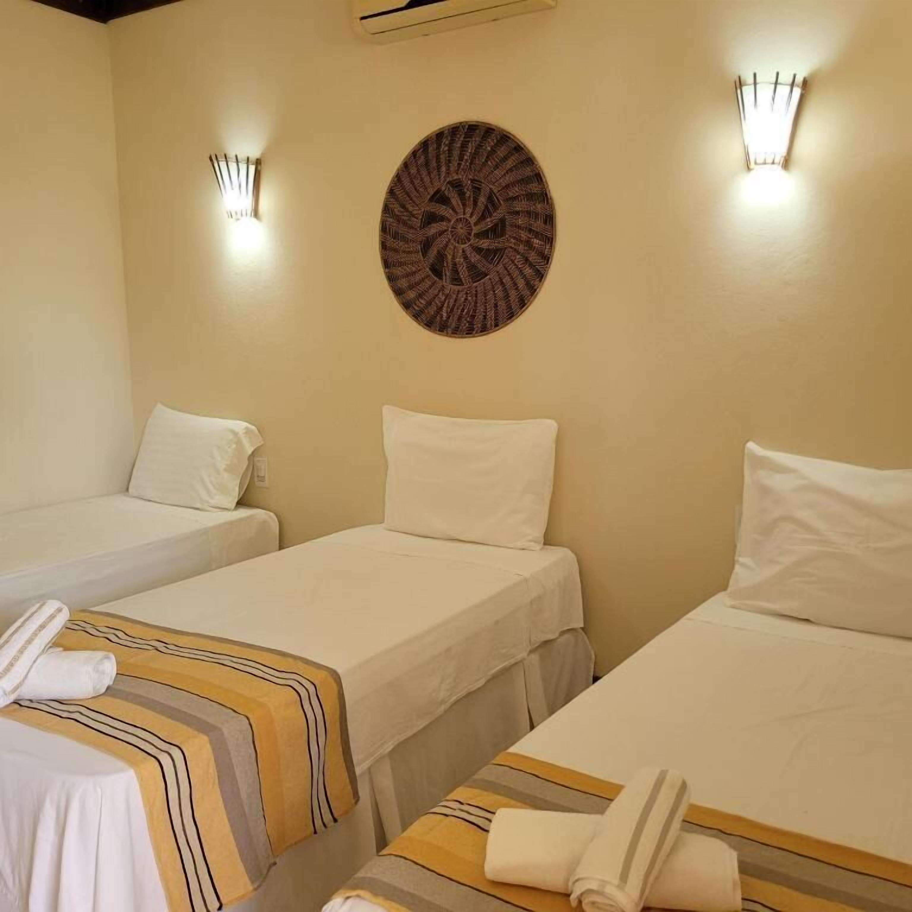 Quarto de hotel com duas camas de solteiro, um ornamento circular na parede e duas luzes fixadas na parede.