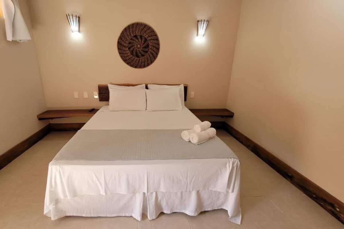 A neatly made bed with white linens and a gray throw blanket, a wooden headboard, and two wall-mounted light fixtures.