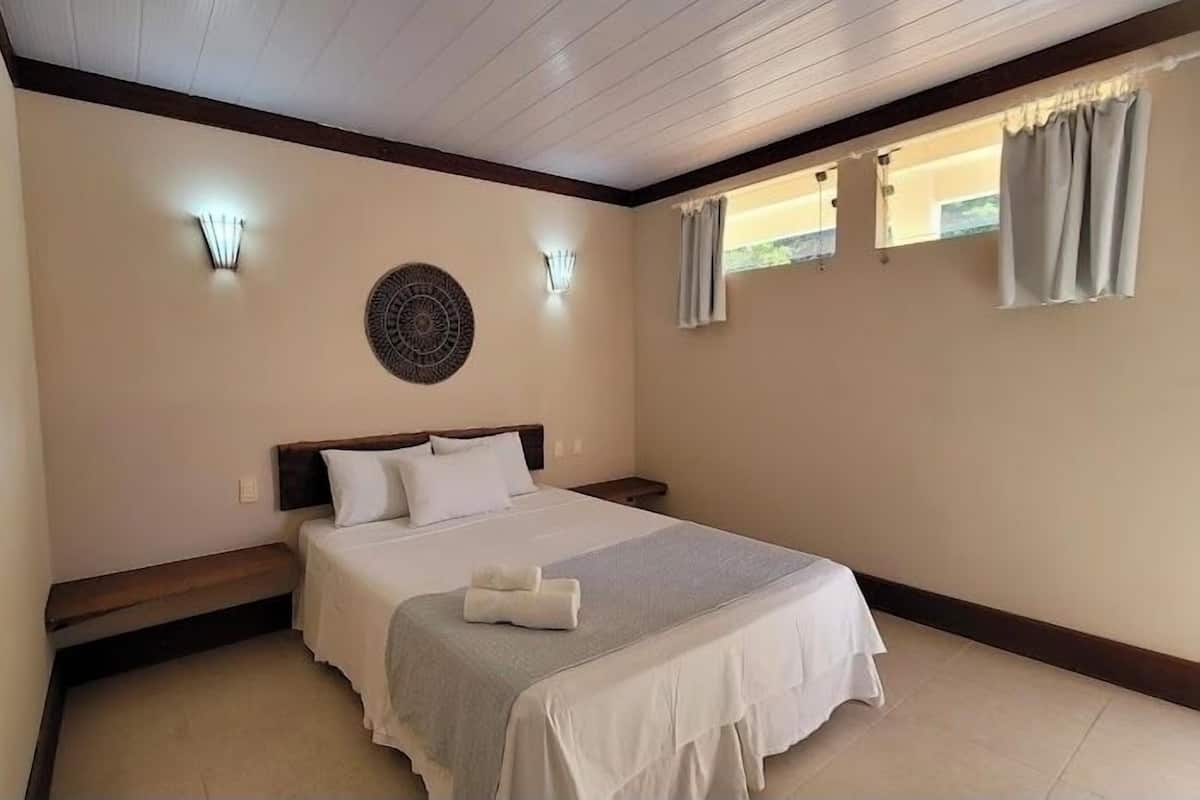 A bedroom with a bed, two wall sconces, a decorative wall piece, and a window with curtains.