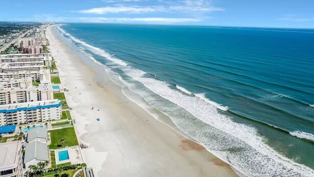 Un hôtel situé sur la côte, avec vue sur la plage, plusieurs piscines et une longue plage de sable.