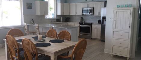 A modern kitchen with white cabinets, a central island, and a dining area with wicker chairs and a wooden table.