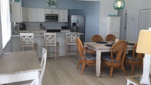 A compact kitchen with white cabinets, a microwave, and a refrigerator. There is a dining area with a wooden table and wicker chairs. - Open Ocean View, Private Hot Tub, Ice Machine, Moor 26' Boat! (Marathon)