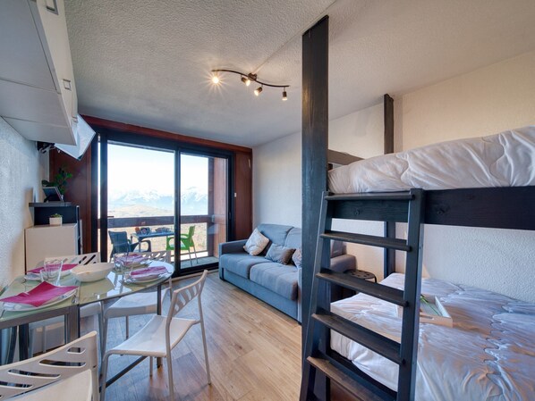 Une pièce compacte comprenant un lit superposé, une table à manger avec des chaises, un canapé et une grande fenêtre donnant sur la montagne.