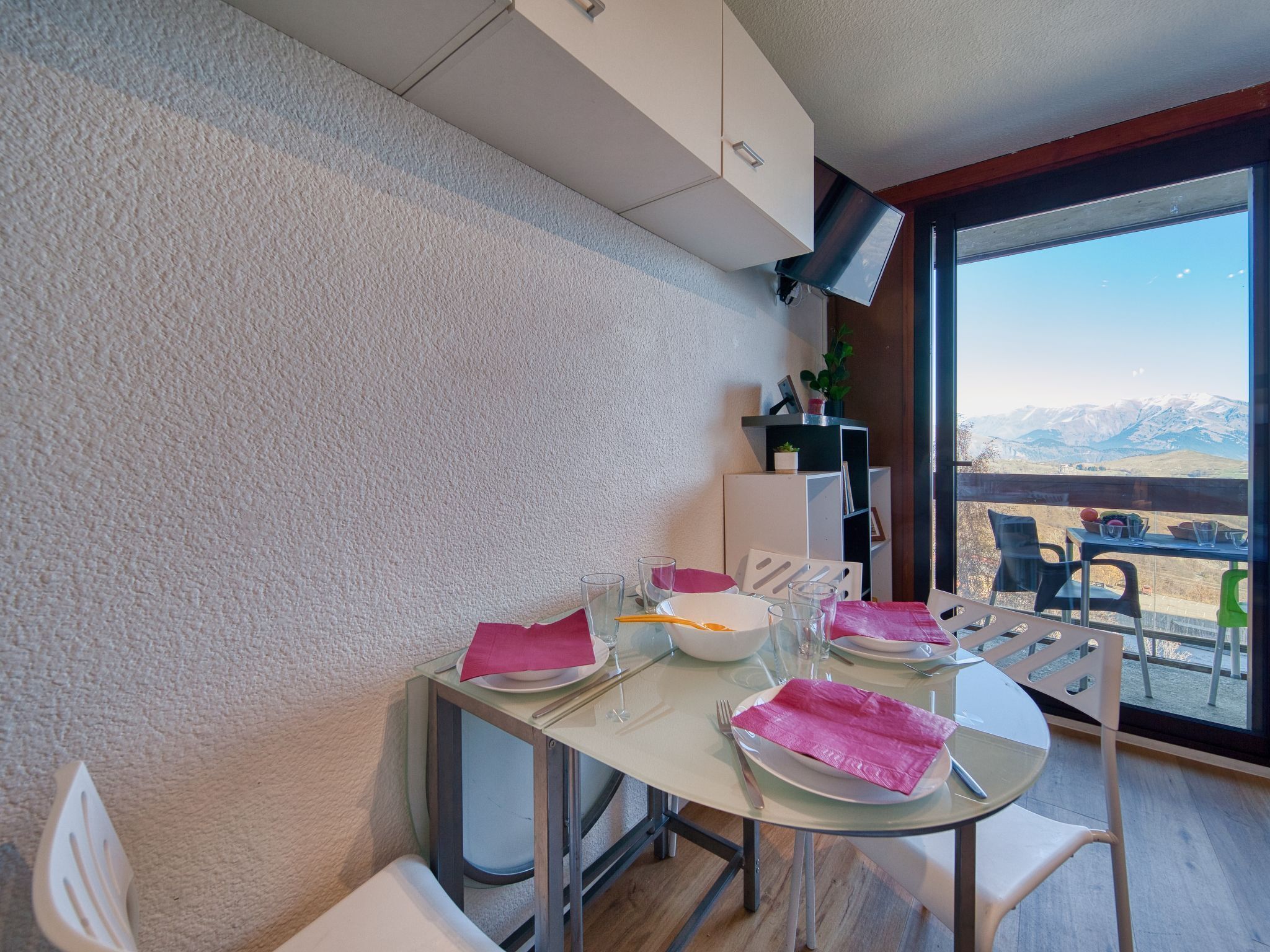 Ein Essbereich mit Tisch für zwei Personen, einem weißen Schrank und Blick auf Berge durch ein großes Fenster.