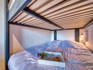 Une pièce confortable avec un lit, un plafond en bois et un luminaire fixé au mur.