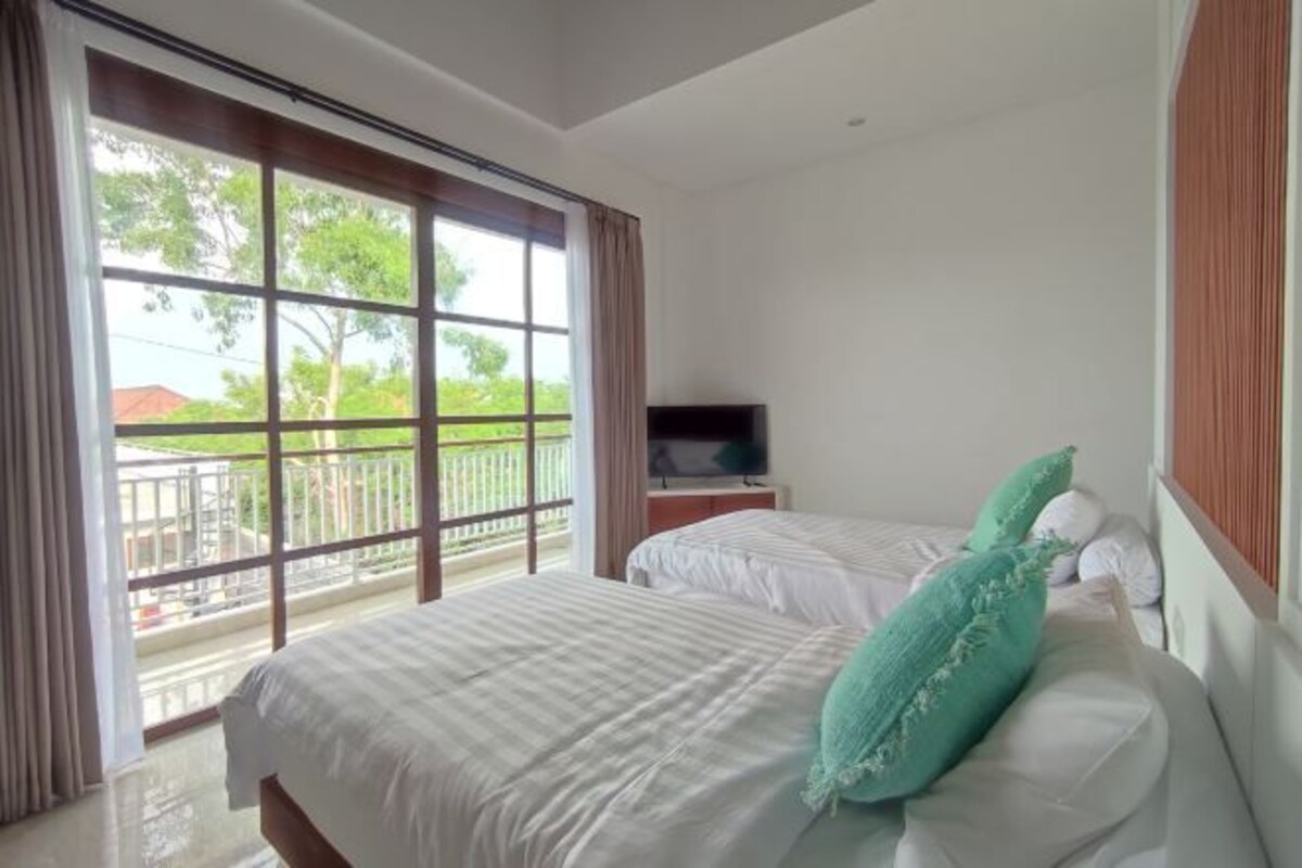 Una camera d'albergo con due letti, una televisione su un comodino in legno e un balcone con ringhiera.