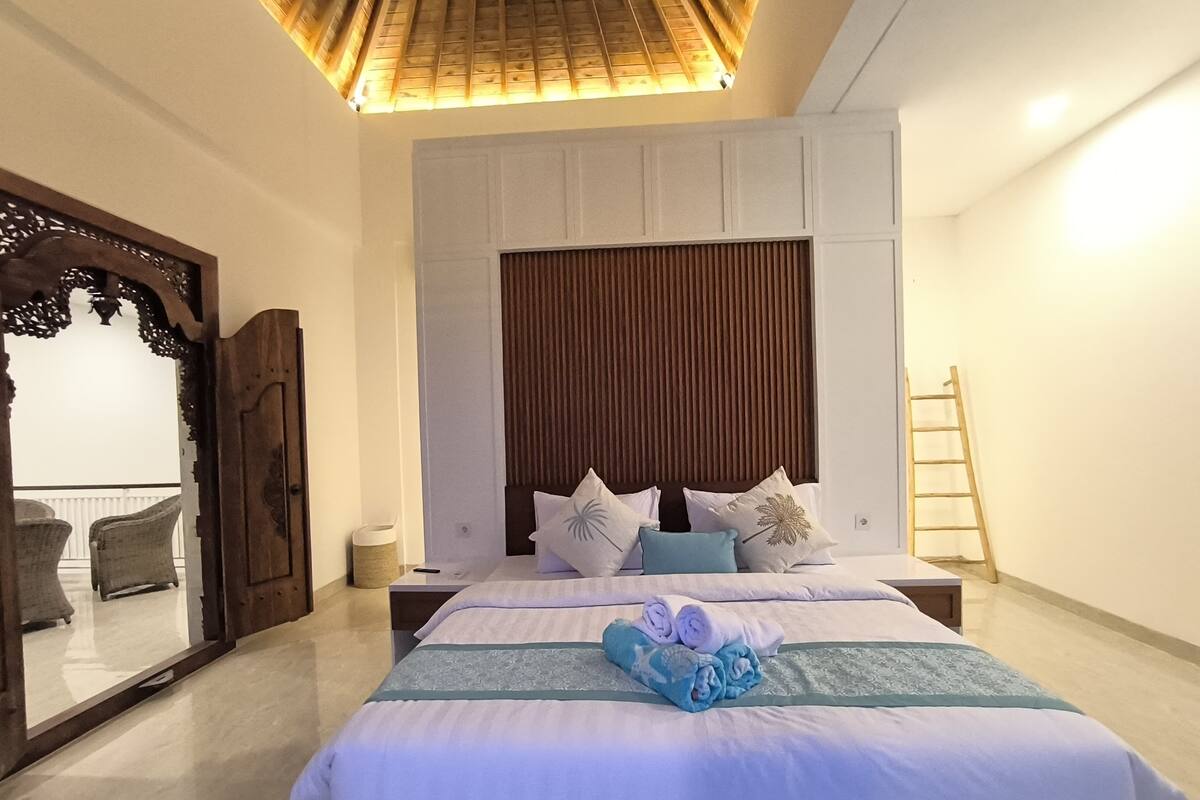 Ein Hotelzimmer mit einem großen Bett, einem Holzkopfstück, einem Spiegel und einer Wandleiter.