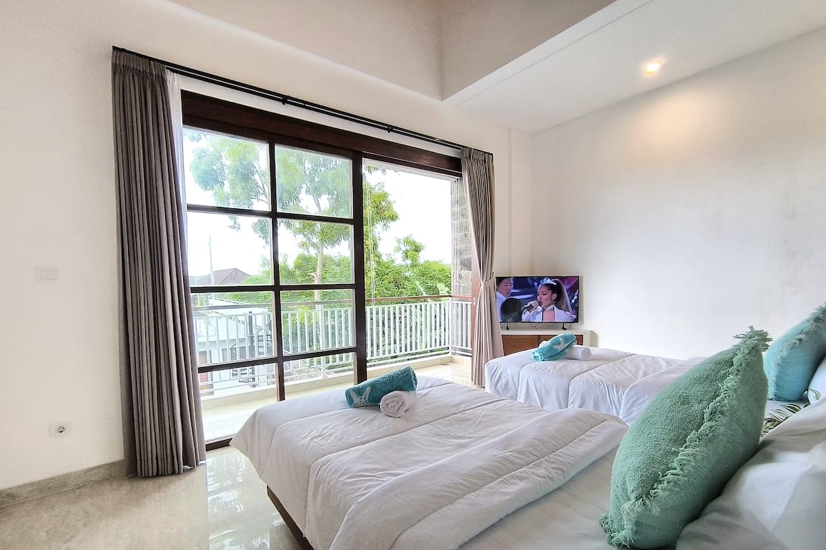 Ein Hotelzimmer mit zwei Betten, einem Fernseher und einem Balkon mit Geländer.