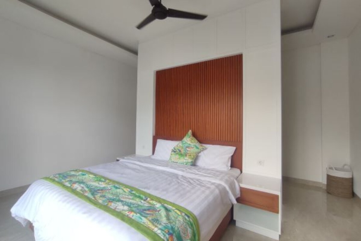 Una camera da letto con un letto, una ventola a soffitto, una testiera in legno e una parete bianca.