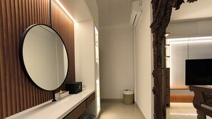 Ein modernes Badezimmer mit einem Holz-Waschtisch, einem runden Spiegel, einem schwarzen Lautsprecher und einem Fernseher.