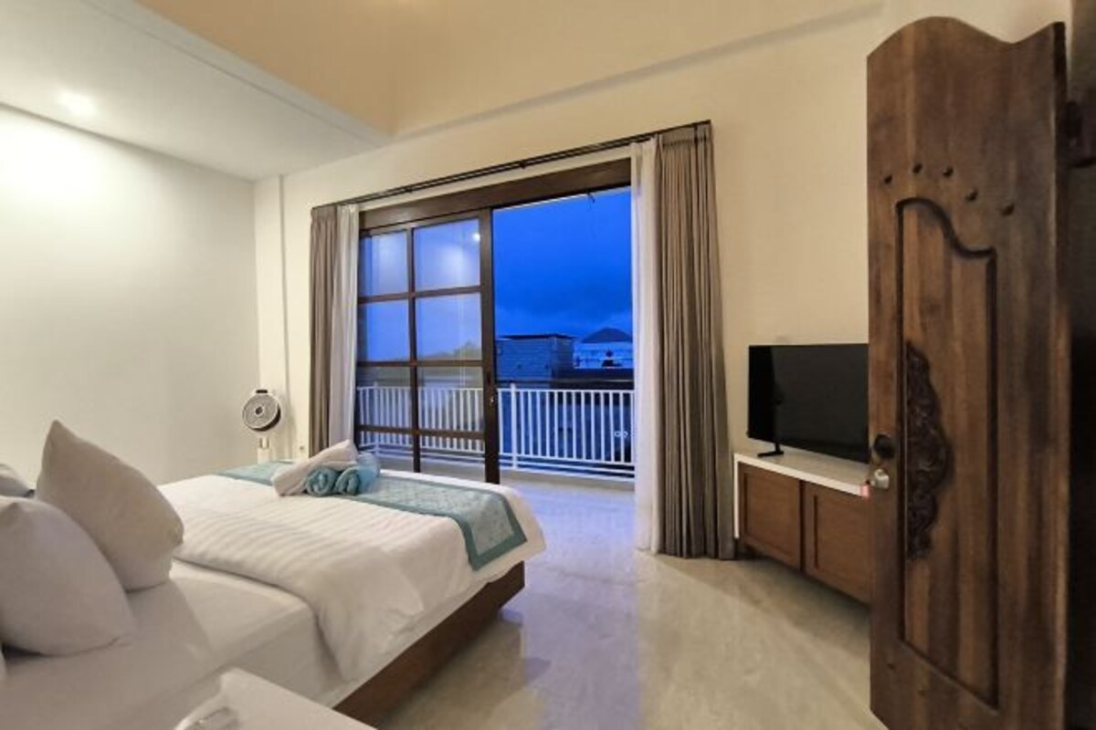 Una camera d'albergo con un letto, una televisione, un armadio in legno e un balcone vista mare.