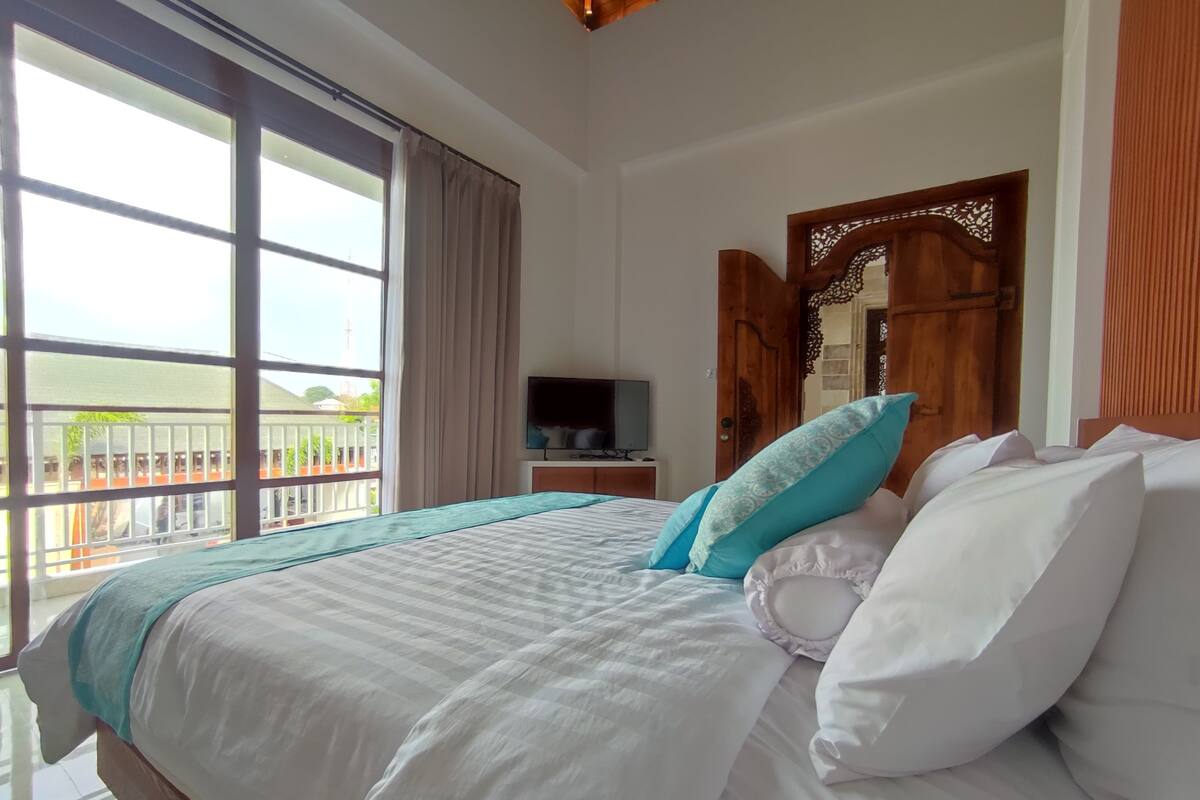 Ein Hotelzimmer mit einem großen Bett, einem Fernseher auf einem Nachttisch aus Holz und einem Balkon mit Geländer.