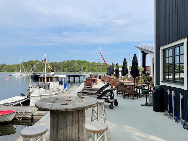 A waterfront restaurant with outdoor seating, a dock with boats, and a view of the lake.