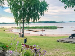 Un parque junto al lago con un muelle de madera, mesas de picnic y una banca.