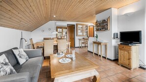 A cozy living room with a wooden ceiling, a grey sofa, a wooden coffee table, and a television on a wooden cabinet.
