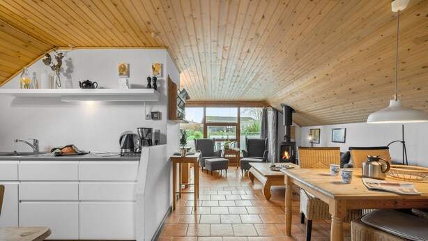 A cozy kitchen with a dining area, wooden ceiling, and a fireplace.
