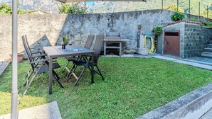 A patio with a table and chairs, a barbecue grill, and a stone wall. - Rolando by Interhome (Lago di Mezzola)