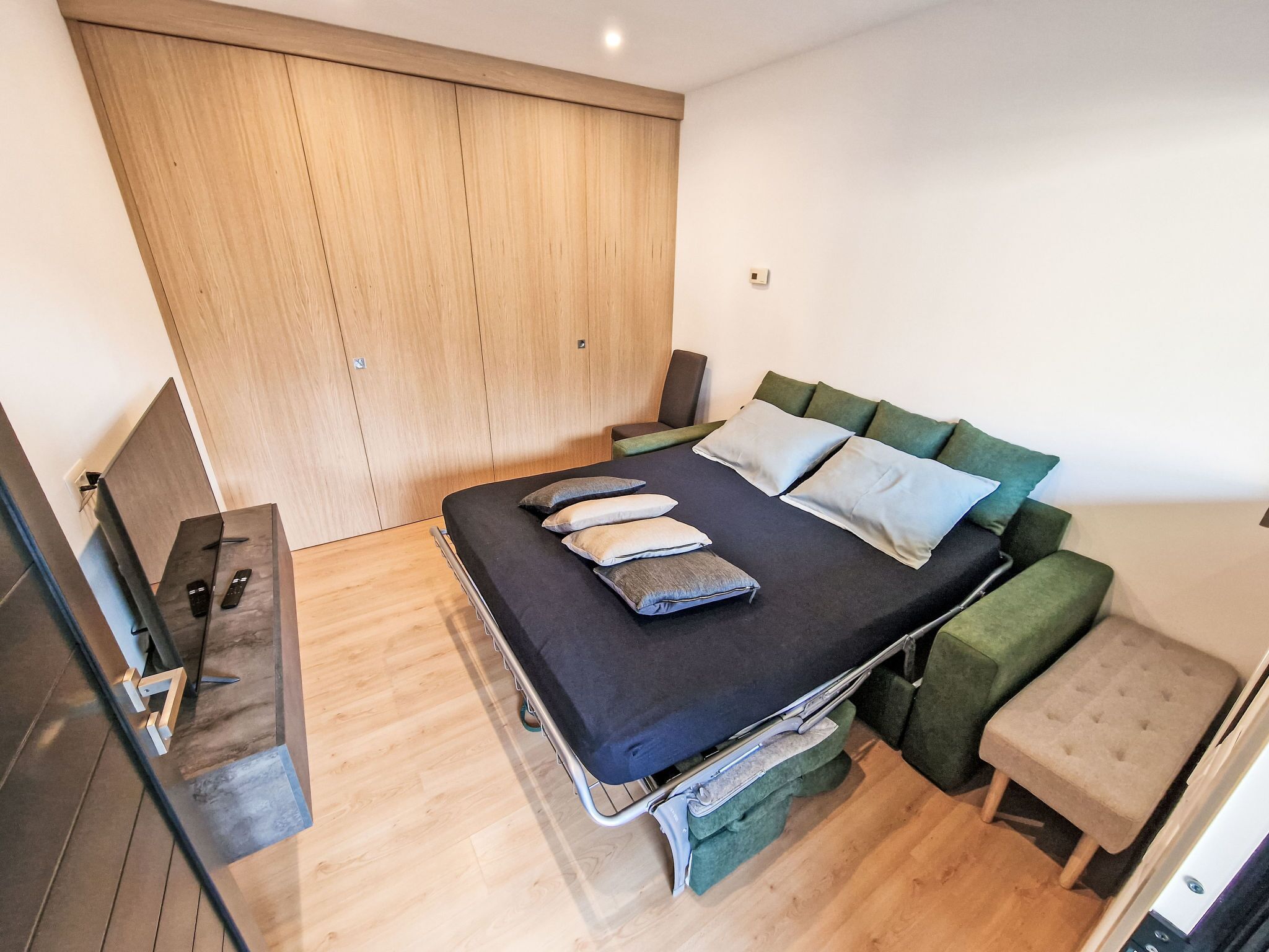 Un dormitorio moderno con cama, mesitas de noche, una silla verde y un taburete pequeño.
