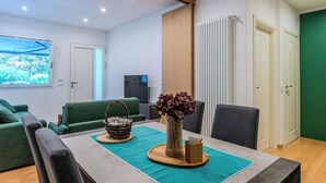 A modern living room with a dining table, green sofa, and a TV. - Rolando by Interhome (Lago di Mezzola)