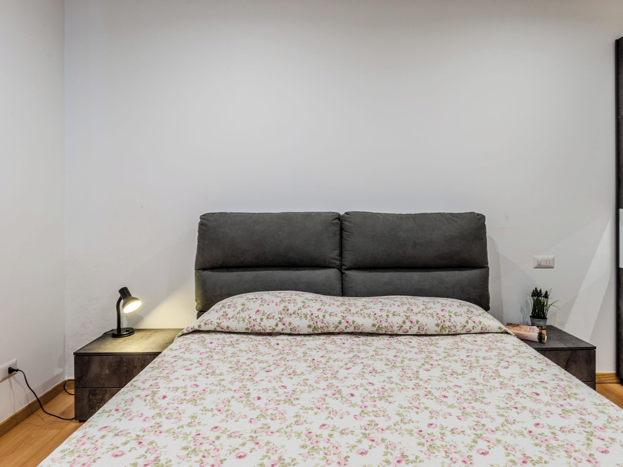 Une chambre à coucher avec un lit, une table de chevet, une lampe et une petite plante en pot.