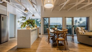 Ett modernt kök med en central köksö, en matplats med trästolar och en stor skjutdörr i glas som leder ut till en balkong med utsikt.