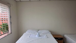 Habitació individual amb un llit, una finestra, una taula de nit i una làmpada penjant de la paret.