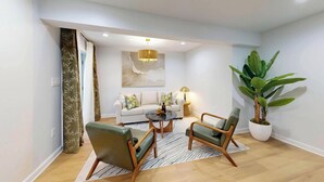 Ein modernes Wohnzimmer mit einer Couch, zwei Sesseln, einem Couchtisch, einer Kronleuchter und einer großen Topfpflanze.