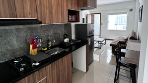 Een moderne keuken met donkere houten kastjes, een zwart aanrecht en roestvrijstalen apparatuur. Er is een zithoek met een bank en een tafel.
