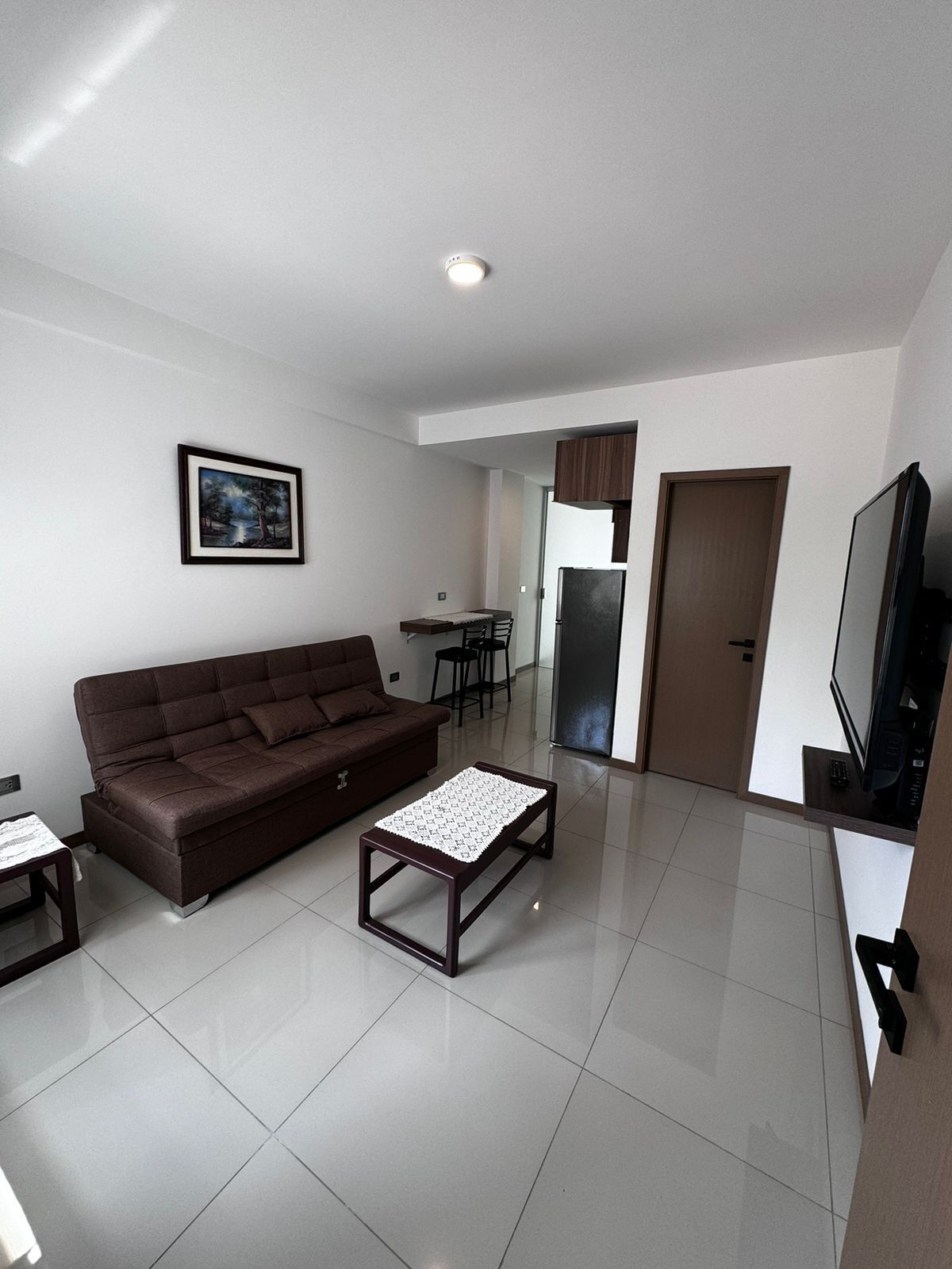 A modern living room with a brown sofa, a coffee table, a TV, and a framed picture on the wall.