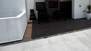 Een modern terras buiten met een ingebouwde open haard, zitplaatsen en een potplant.