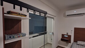 Een moderne slaapkamer met een inloopkast met glazen schuifdeuren, een bed met beddengoed met een patroon, en een wandairconditioning.