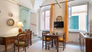 A dining area with a table and chairs, a television mounted on the wall, and a window with curtains. - Casa della Mamma by Interhome (Riva Ligure)