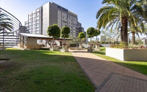 A courtyard with a pathway, palm trees, and a building with multiple floors.