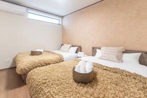 Hotellihuone, jossa on kaksi sänkyä, ikkuna, seinään asennettu ilmastointilaite ja yöpöytä, jossa on lamppu.