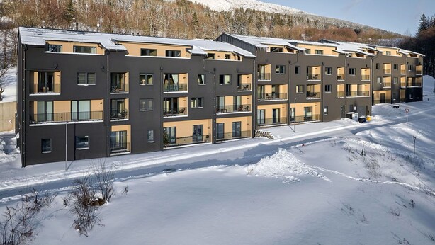 A multi-story apartment building with balconies, set in a snowy landscape with a forested hill in the background. - Nice apartment for 4 people with WIFI, TV and terrace (Vrchlabí)