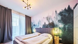 A bedroom with a bed, a headboard, a nightstand, a wall mural, and a window with curtains. - Nice apartment for 4 people with WIFI, TV and terrace (Vrchlabí)