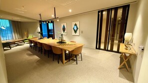 Een moderne eetruimte met een lange houten tafel, diverse stoelen en een bijzettafeltje met een lamp.