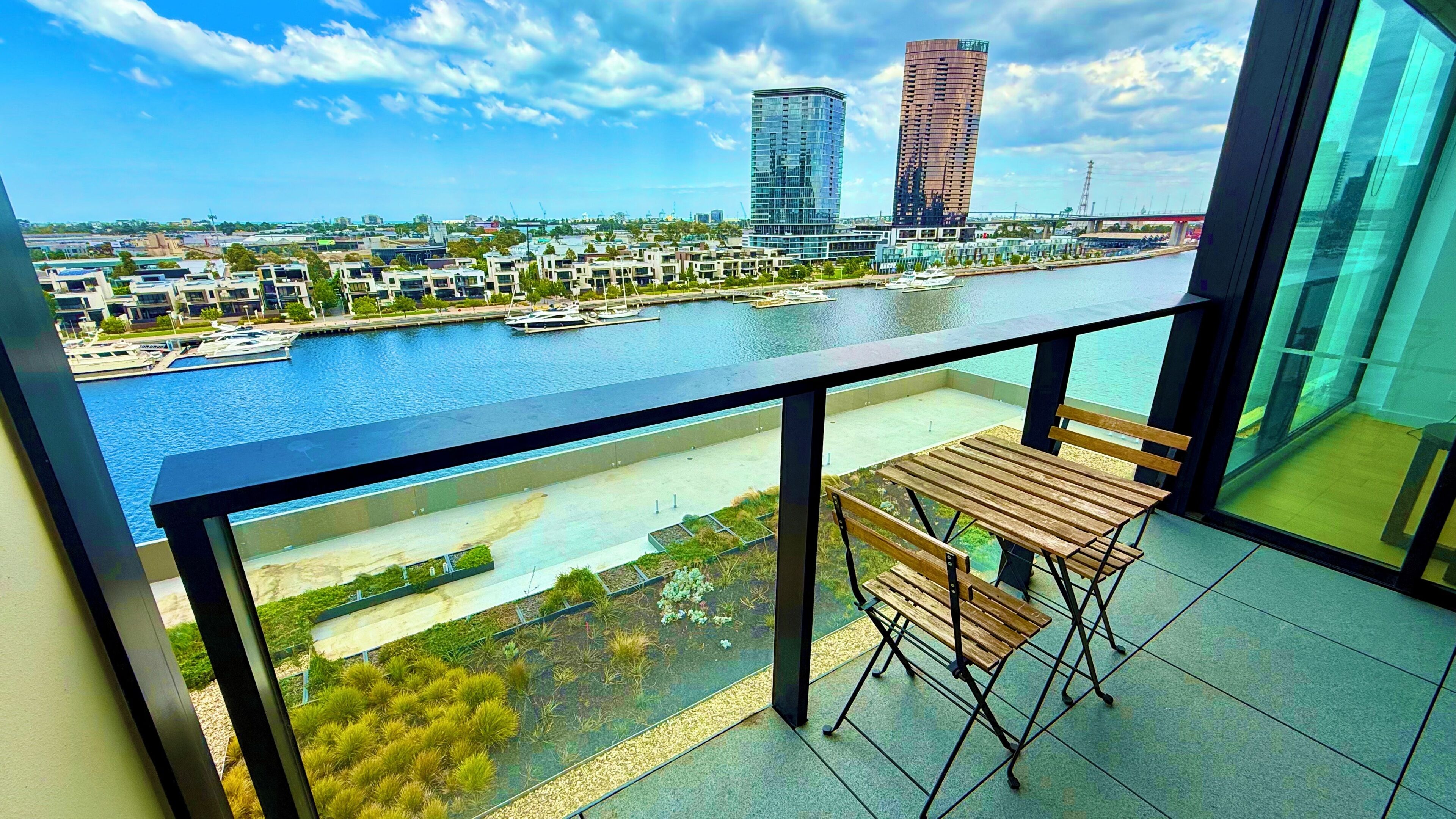 Un balcon avec vue sur un port de plaisance, des bâtiments modernes et une rivière.