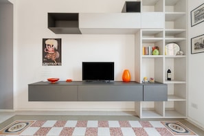 A modern living room with a flat-screen TV, a grey console, and a patterned rug.