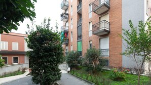 A multi-story residential building with balconies, a paved courtyard, and surrounding greenery.