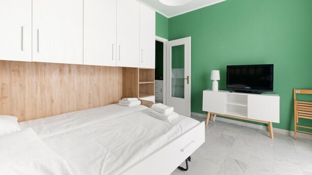 A modern bedroom with a bed, white wardrobe, TV, and a green wall.