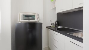 A compact kitchen with a black refrigerator, a white microwave, a black countertop, and white cabinets.