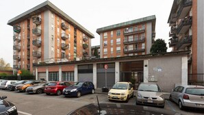A multi-story residential building with balconies, a parking area, and a no parking sign.